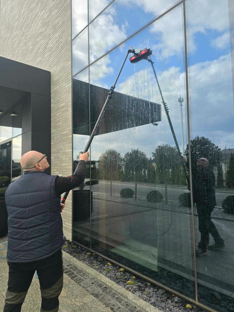 Pracownik myjący szklaną elewację i duże przeszklenia budynku kijem teleskopowym z wodą demineralizowaną